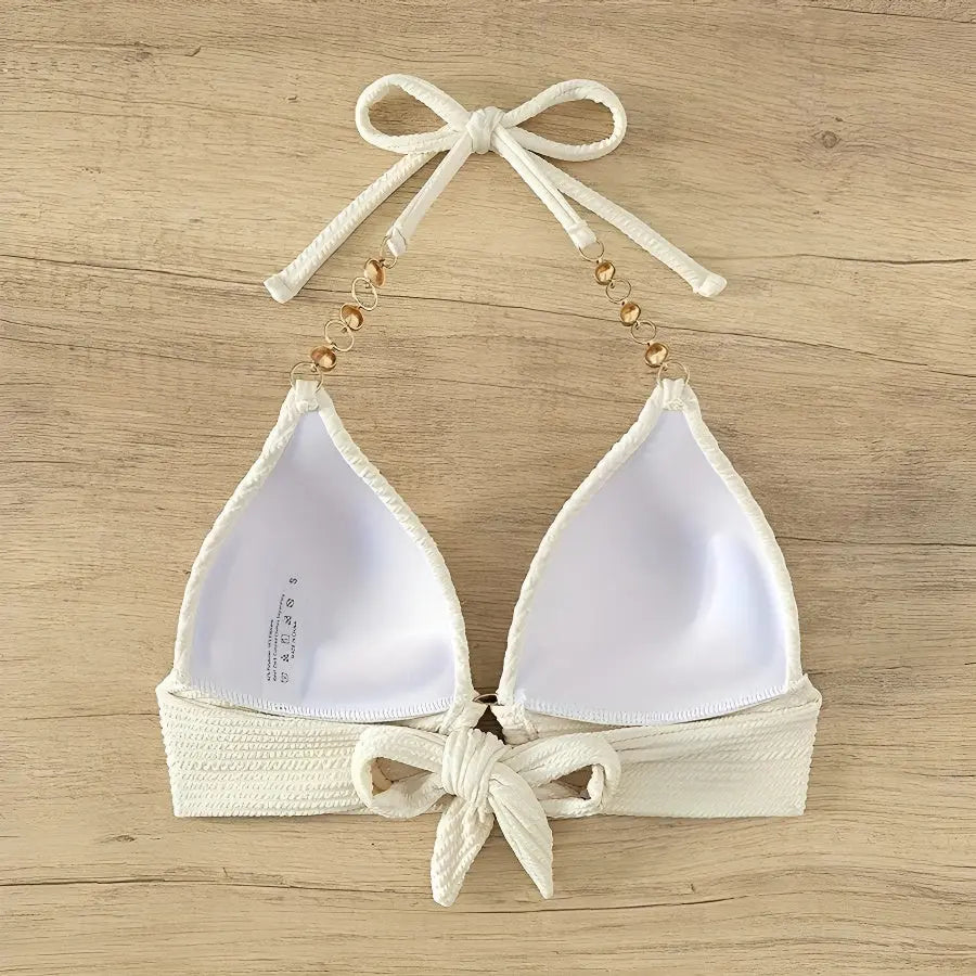 White bikini top with beige straps and bows on a wooden surface